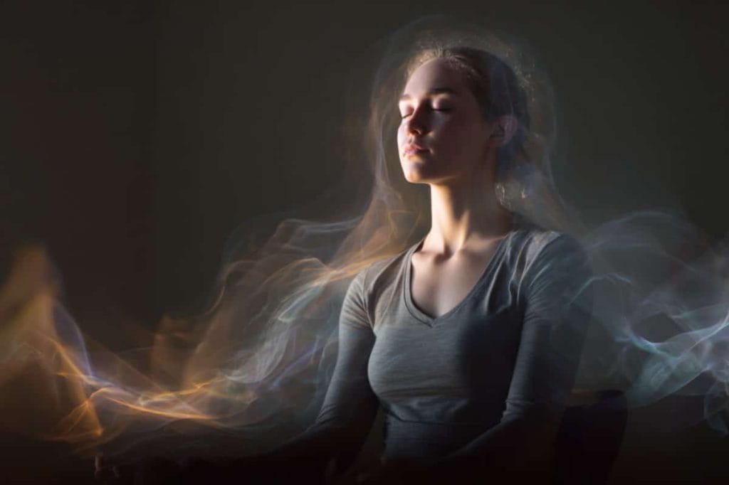 This shows a woman in a meditative pose with a small device on her ear. She looks at peace and is surrounded by waves.