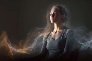 This shows a woman in a meditative pose with a small device on her ear. She looks at peace and is surrounded by waves.